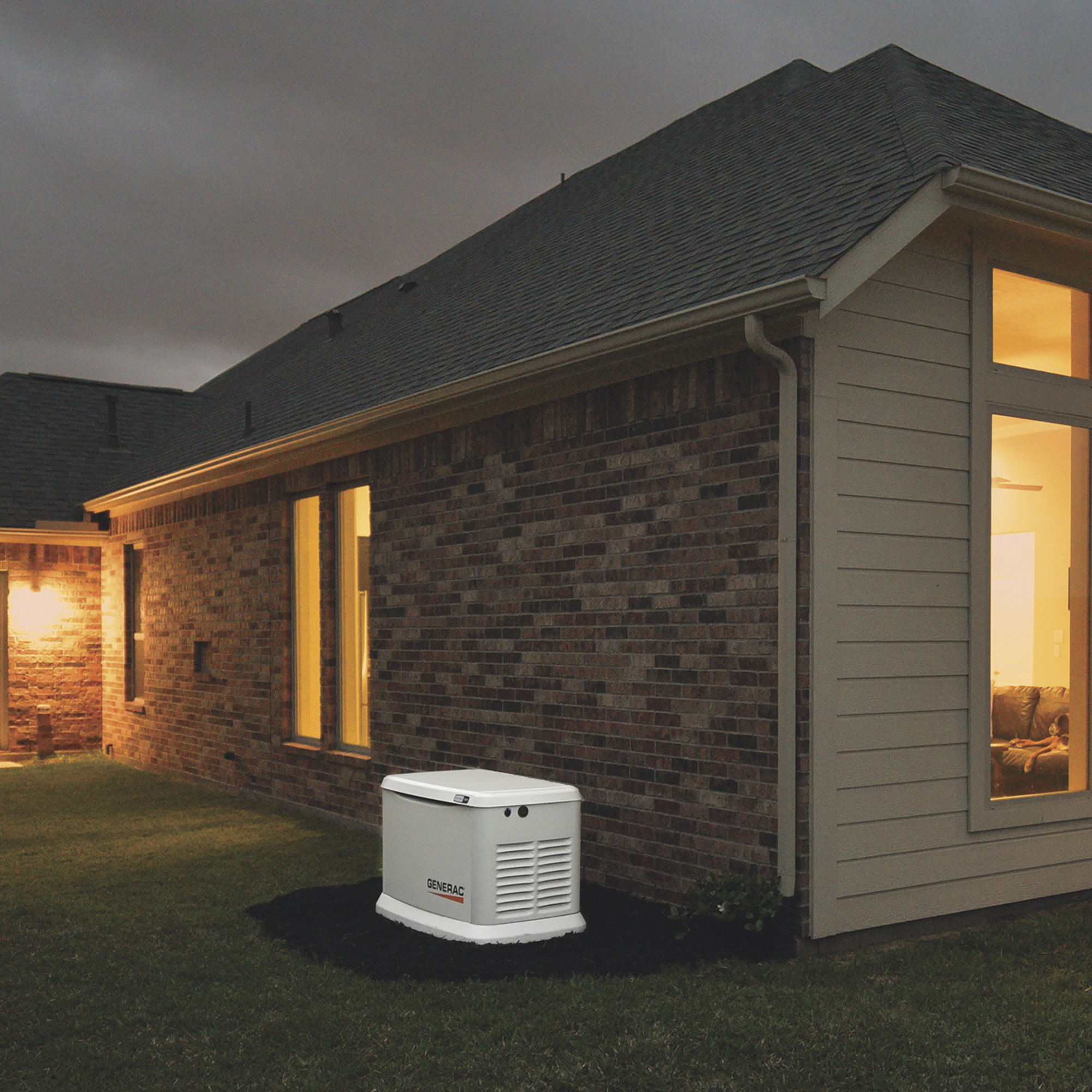 Generac Home Standby Generator next to a home lit up from inside